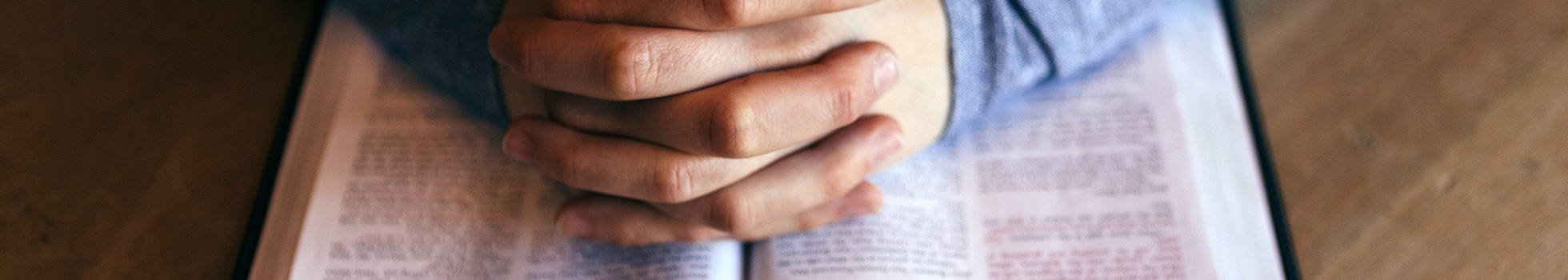 Hands praying over a Bible.