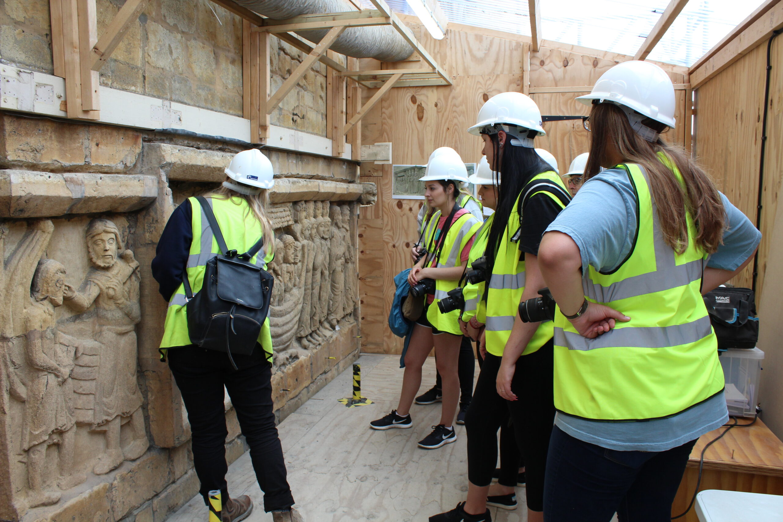 Students in hard hats and yellow safety vests gathered around art work.