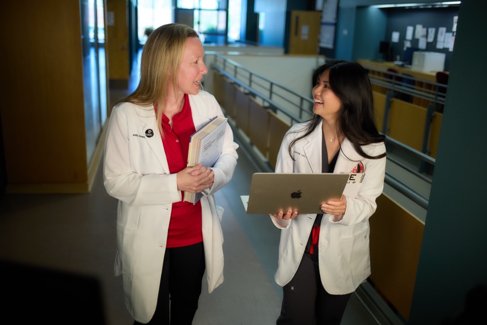 Two Drury PA students walking in a dimly lit hall side by side, having a conversation.