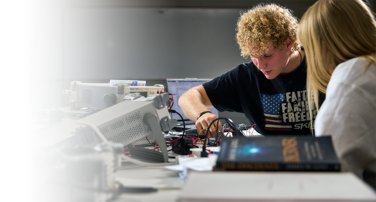 two drury engineering students, one blonde curly haired male and a blond straight hair female, work on an electronic project they've built together.