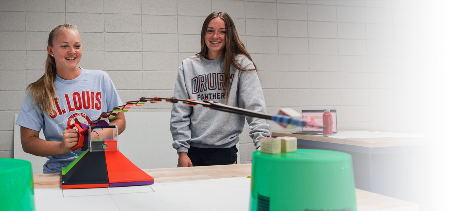 two female drury engineering students playing with a extending arm toy they built in the lab.