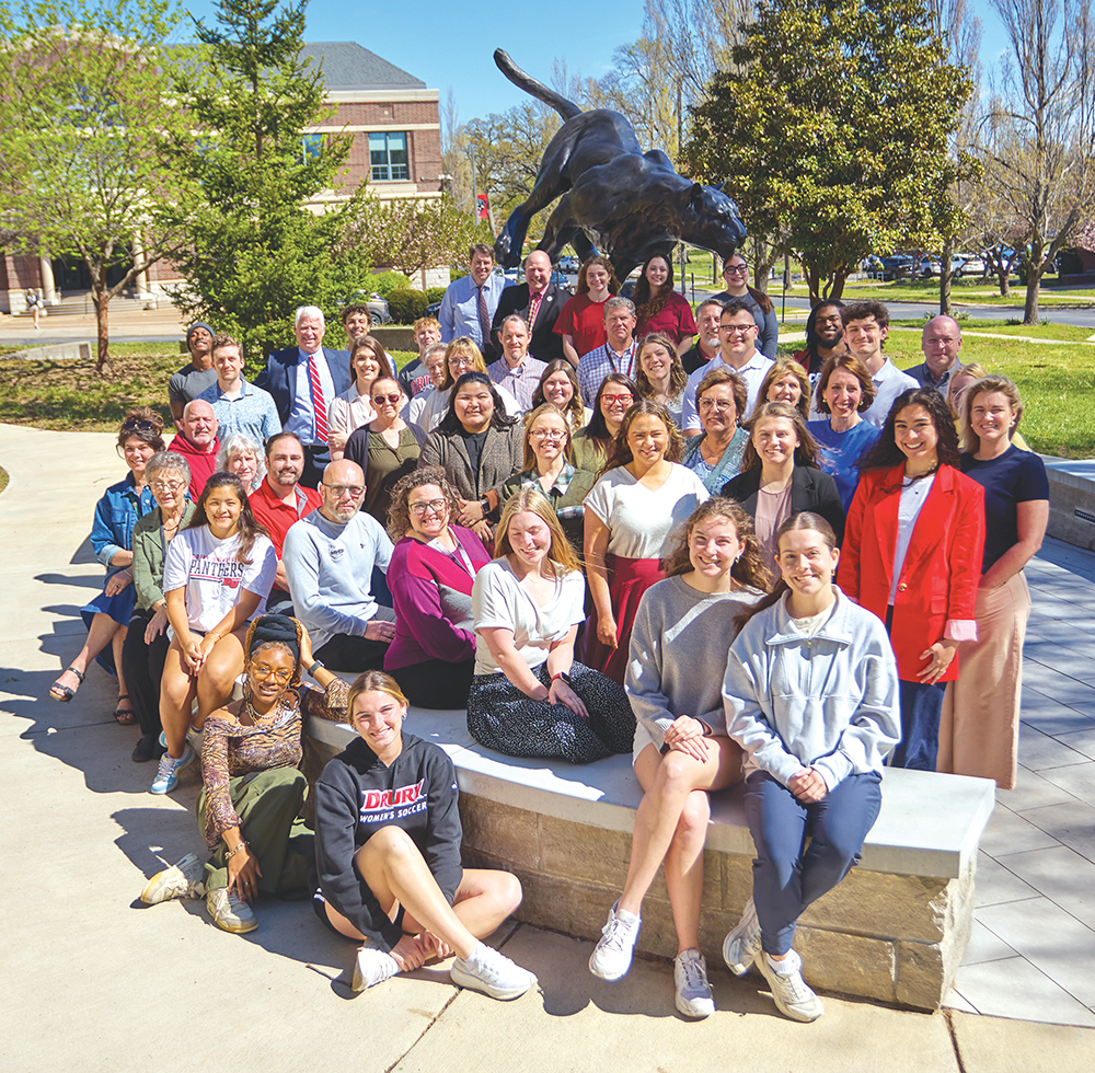 A group of Drury faculty, staff, and students gathered around the Panther statue located in the heart of campus, on a sunny Spring morning in Springfield, Missouri.